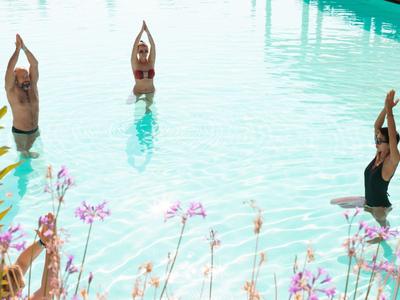 Trzy osoby ćwiczące jogę w czystym niebieskim basenie z kwiatami na pierwszym planie.