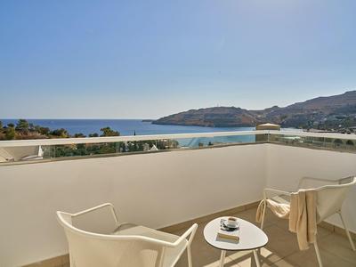 Balkon mit weißem Geländer, zwei Stühlen und kleinem runden Tisch, Meerblick und Hügel im Hintergrund.