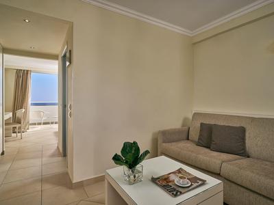 Kleines Wohnzimmer mit grauem Sofa, weißem Tisch und Blick auf Terrasse mit Meer im Hintergrund.