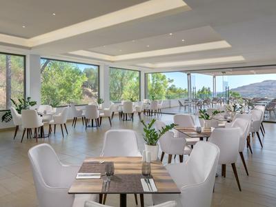 Helles Hotelrestaurant mit weißen Stühlen, Holztischen und großen Fenstern mit Bergblick.