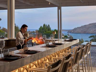 Nowoczesna przestrzeń na zewnątrz z otwartą kuchnią, paleniskiem i widokiem na morze o zmierzchu.