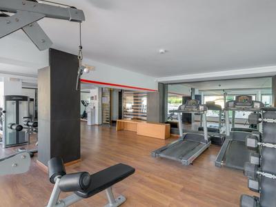 Jasna siłownia z urządzeniami cardio i maszynami siłowymi na drewnianej podłodze.