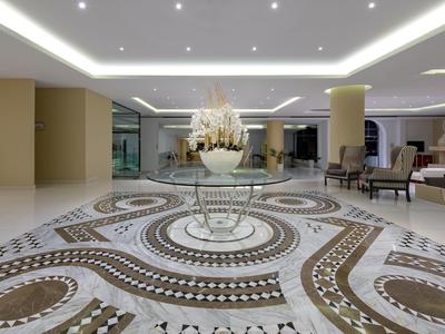 Helles, modernes Hotel-Foyer mit kunstvollem Mosaikboden und sitzbereitgemachten Sesseln.
