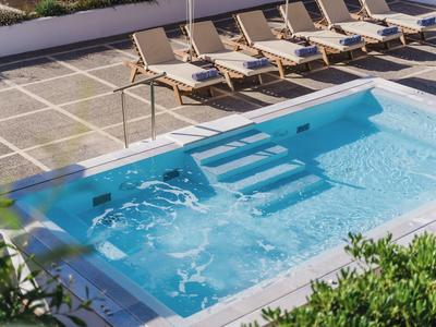 Kleiner rechteckiger Pool mit klar blauem Wasser, Treppen und sechs Liegestühlen auf grauem Boden.