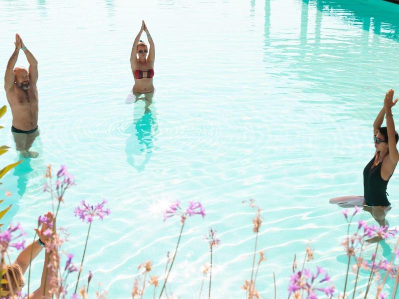 Drei Personen stehen im Wasser und machen synchrones Yoga mit erhobenen Armen.