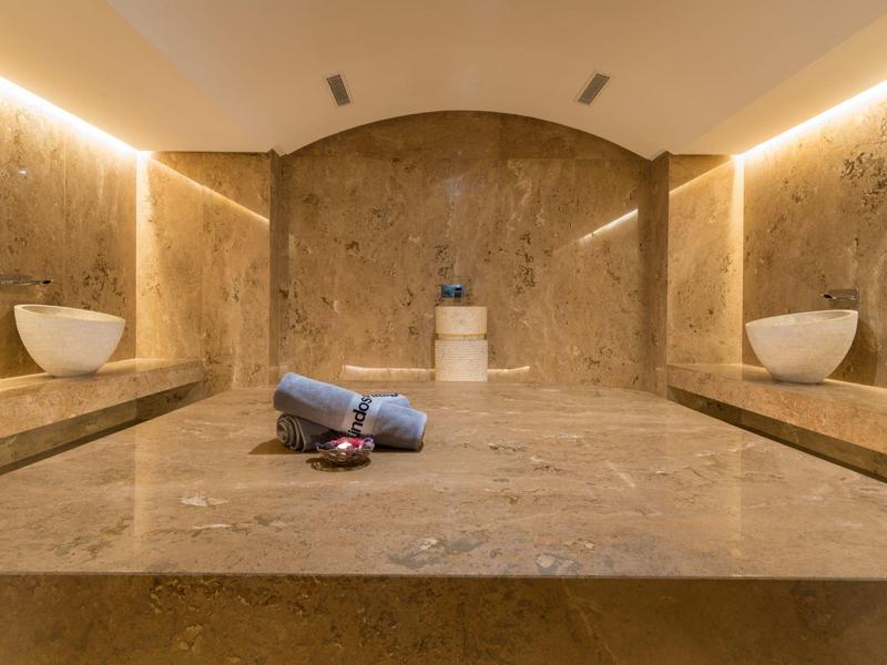 Moderner Spa-Raum mit Sandsteinwänden, zwei weißen Becken und einem grauen Handtuch auf der Arbeitsplatte.