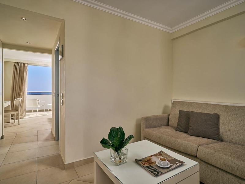 Kleines Wohnzimmer mit grauem Sofa, weißem Tisch und Blick auf Terrasse mit Meer im Hintergrund.