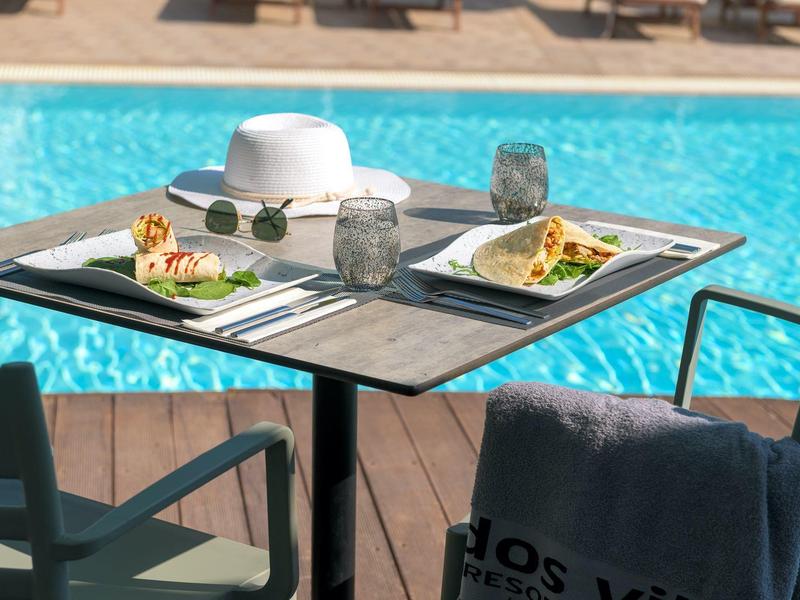 Tisch mit zwei Tacos und Getränken an einem Pool mit zwei Stühlen und Sonnenhut.