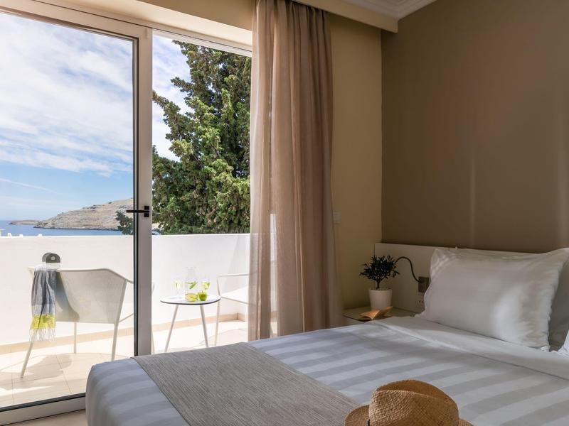 Helles Schlafzimmer mit großem Bett, Balkon, weißen Vorhängen und Blick auf Berge und Meer.