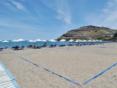 Sandiger Strand mit Volleyballfeld, Sonnenschirmen und Stühlen unter blauem Himmel.