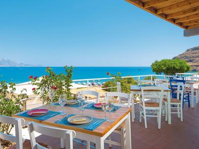 Terrassenrestaurant mit blauen Tischen, weißen Stühlen und Meerblick unter blauem Himmel.