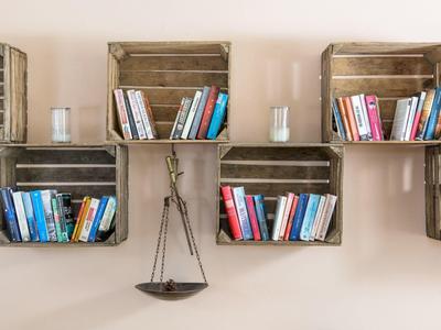Wandregal aus Holzboxen mit bunten Büchern und zwei kleinen weißen Kerzenhalter.