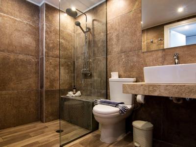 Modernes Badezimmer mit braunen Fliesen, Glasdusche, weißem WC und elegantem Waschbecken.