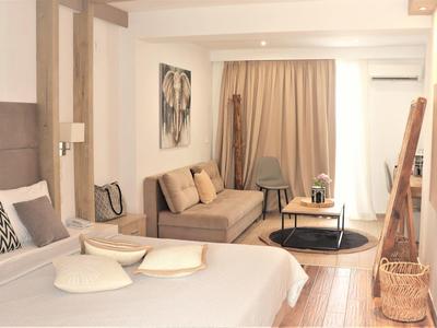 Hell eingerichtetes Schlafzimmer mit Bett, Sofa, Vorhang, Wandbild und TV an der Wand.