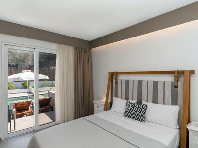 Modernes Schlafzimmer mit Doppelbett, grauen Wänden, Vorhängen und Zugang zu Terrasse mit Sitzbereich.