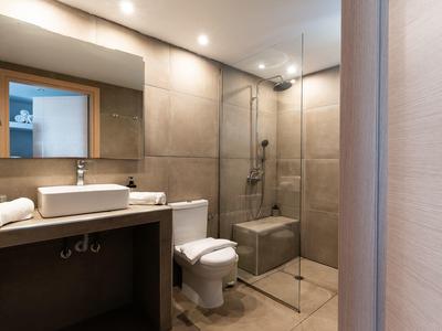Helles Bad mit großer Dusche, weißem WC, Waschbecken auf Holzunterschrank und rechteckigem Spiegel.