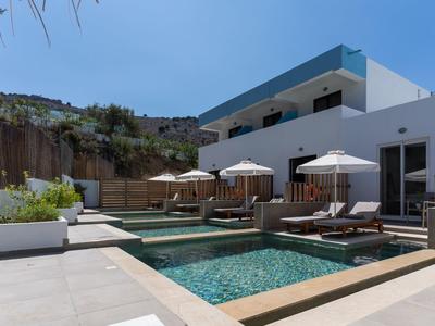 Moderner Poolbereich mit Sitzgelegenheiten und Sonnenschirmen vor weißem Gebäude unter blauem Himmel.