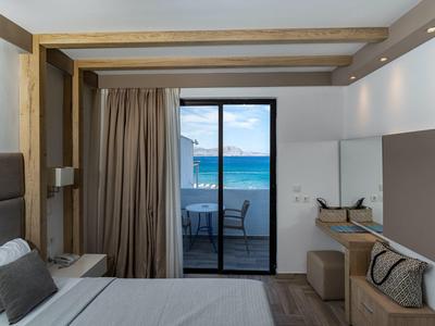 Modernes Hotelzimmer mit Bett, Holzbalken, Schreibtisch und Meerblick durch Glasschiebetür.
