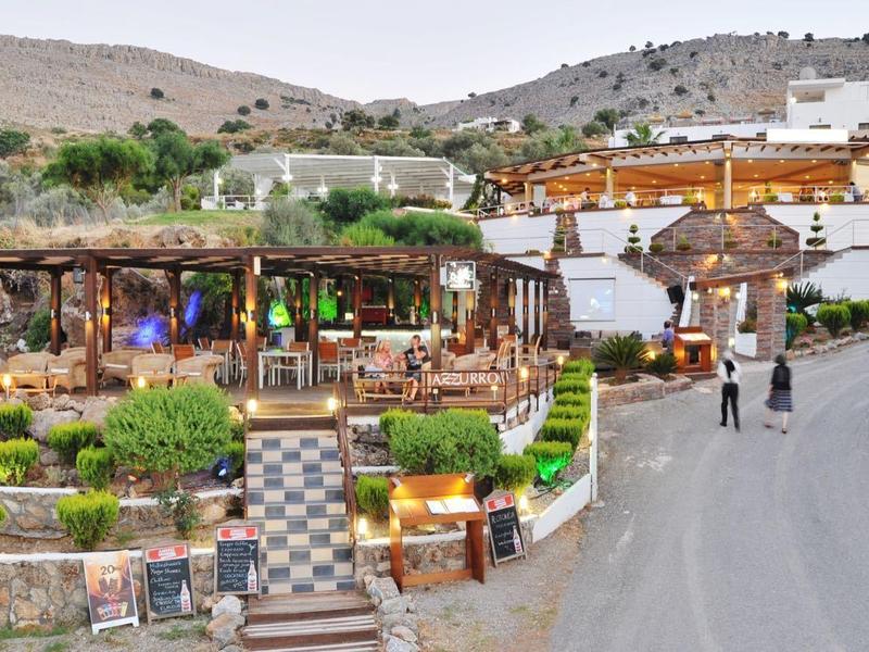 Ristorante con terrazza e piante in un paesaggio collinare accanto a una strada.