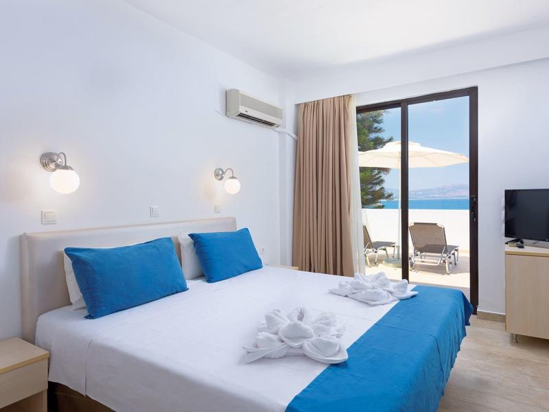 Camera d'hotel moderna con letto matrimoniale, biancheria blu e bianca e vista mare.