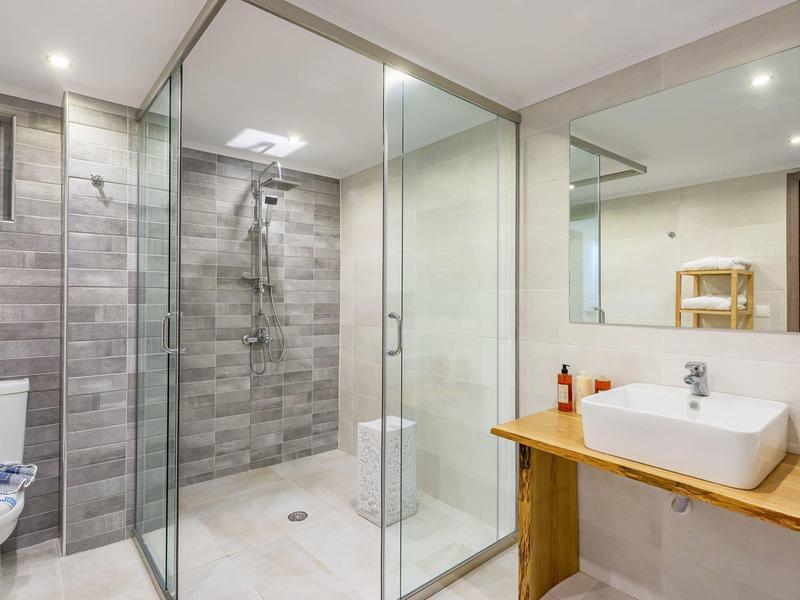 Bagno moderno con doccia walk-in in vetro e lavabo su mobile in legno.