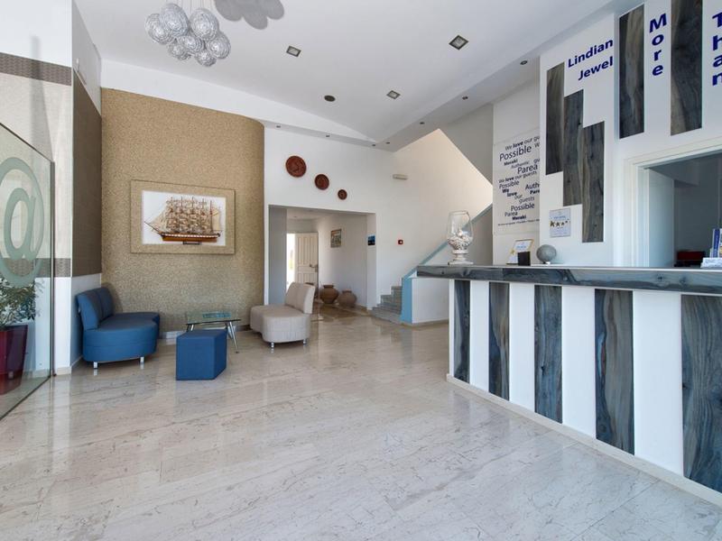 Area reception d'hotel luminosa con banco moderno, scala e posti a sedere.