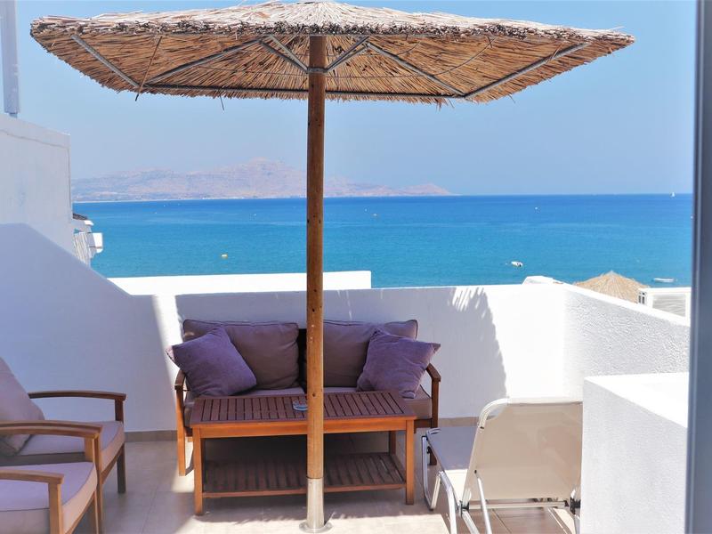 Balcone con sedie e divano sotto ombrellone con vista sul mare e sul cielo.