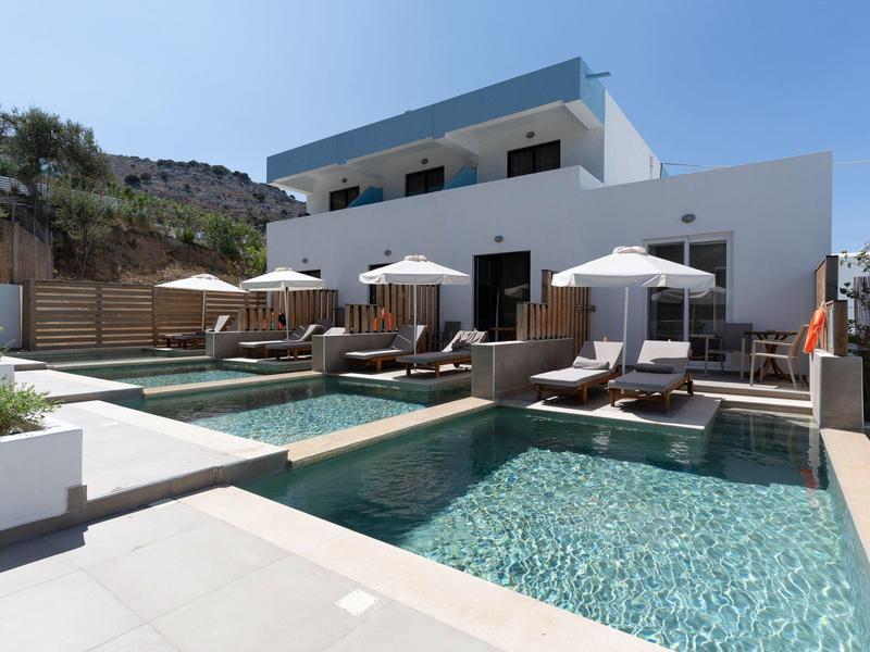 Hotel moderno con due piccole piscine e lettini sotto ombrelloni.