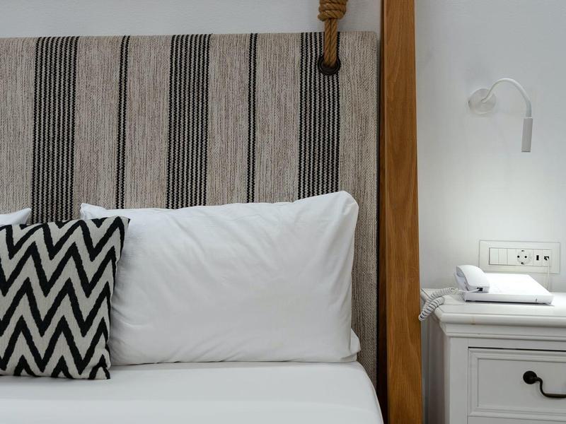 Letto moderno con struttura in legno, cuscini bianchi e cuscino decorativo accanto a comodino con lampada.