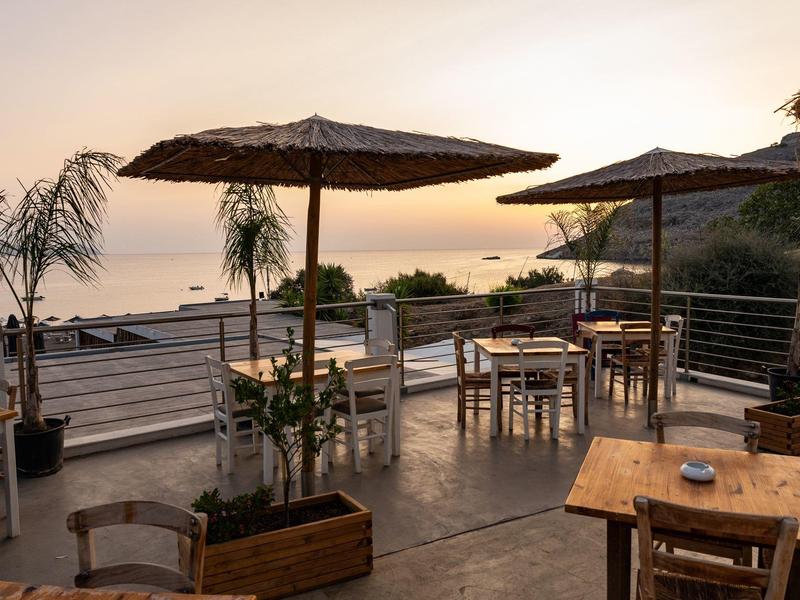 Terrazza con tavoli e ombrelloni con vista sul mare al tramonto.