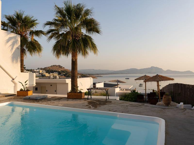 Piscina con palme e lettini con vista mare al tramonto.