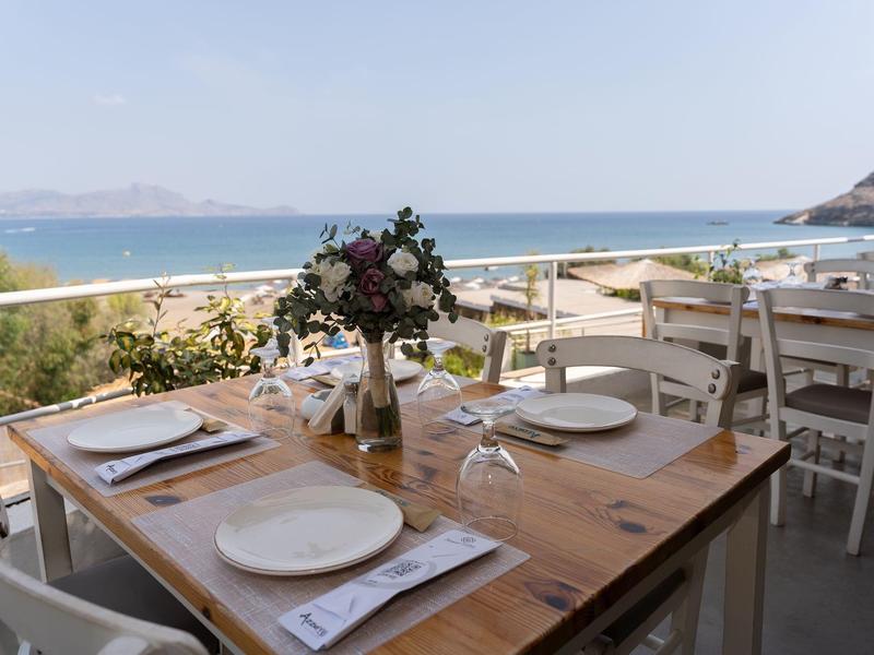 Tavolo apparecchiato con piatti e fiori su terrazza con vista mare.