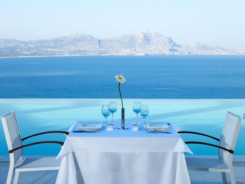Ein gedeckter Tisch mit weißem Tuch und Gläsern auf einer Terrasse mit Meerblick.