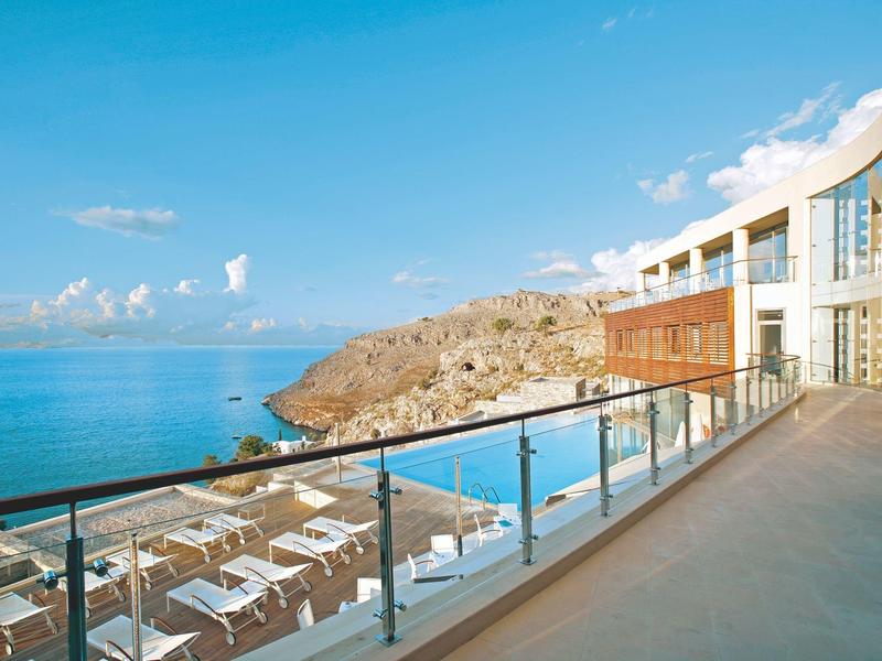 Balkon mit Glasgeländer und Blick auf das Meer und einen Klippenstrand bei klarem Himmel.