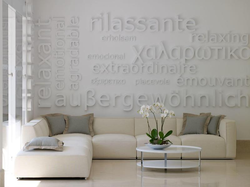 Helles, modernes Wohnzimmer mit weißem Ecksofa, rundem Glastisch und dekorativer Pflanzen- und Wandgestaltung.