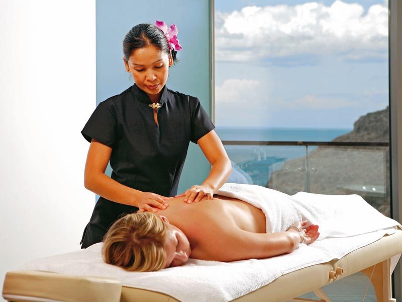 Eine Frau erhält eine Rückenmassage in einem hellen Raum mit Aussicht auf Meer und Himmel.