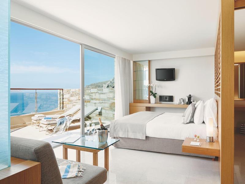 Modernes Hotelzimmer mit Meerblick, Doppelbett und Terrasse mit Sonnenliegen.