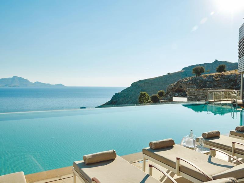 Infinity-Pool mit Sonnenliegen und Blick auf das Meer und die Berge.