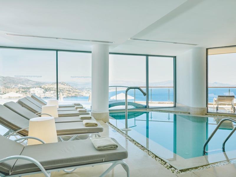 Moderner Innenpool mit weißen Liegestühlen und großem Panoramafenster mit Meerblick