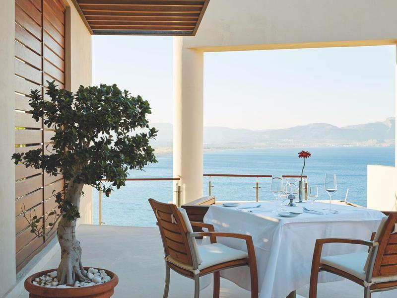 Terrasse mit gedecktem Tisch und Blick auf das ruhige blaue Meer und die Berge im Hintergrund.