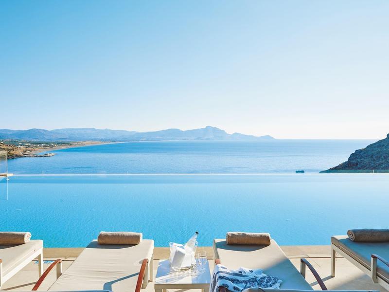 Infinity-Pool mit Sonnenliegen und Meerblick unter klarem Himmel.