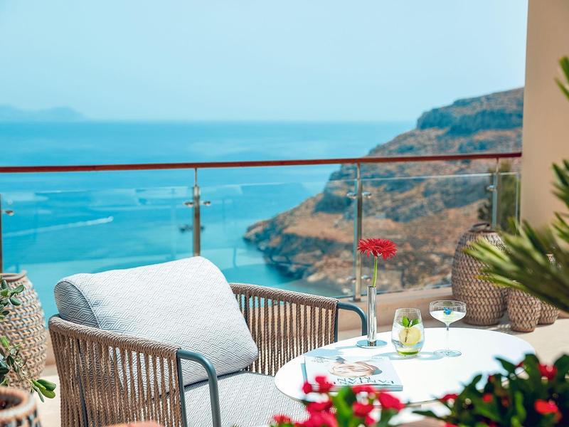 Balkon mit bequemen Sesseln und Tisch, mit Blick auf das Meer und felsige Küste.