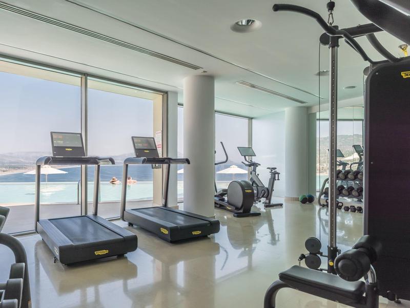 Heller Fitnessraum mit Laufbändern und Trainingsgeräten mit Meerblick durch große Fenster