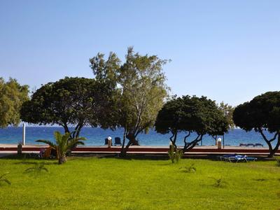 Grüner Park mit Bäumen und Bänken am Meer unter klarem Himmel.