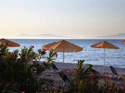 Strand mit Liegestühlen und Sonnenschirmen, Meer und Insel im Hintergrund bei Sonnenuntergang.