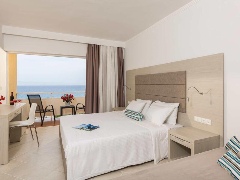 Helles Hotelzimmer mit Doppelbett, Balkon mit Meerblick und schlichtem modernem Mobiliar.