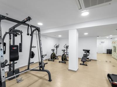 Moderní fitness místnost s vybavením jako lavička, kola a veslovací stroj v světlé místnosti.