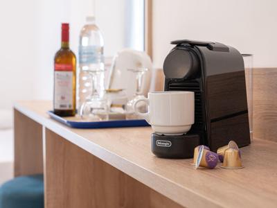 Kaffeemaschine mit Tasse und Kaffeekapseln auf einer Holztheke neben Weinflasche und Wasserflasche.