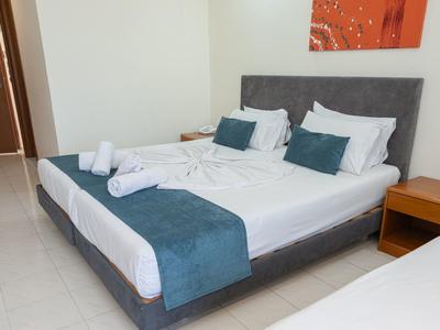 Modernes Hotelzimmer mit einem großen Bett, weißen und blauen Bettwaren und Nachttischen.