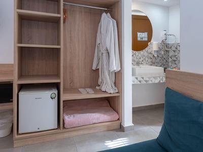 Ein offener Holzschrank mit Bademänteln, Handtüchern und einem kleinen Kühlschrank in einem Hotelzimmer.